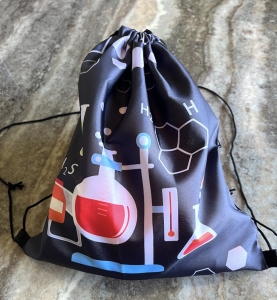 A black drawstring bag decorated with colourful chemistry-themed illustrations, including items in the Bubbleology Science Kit