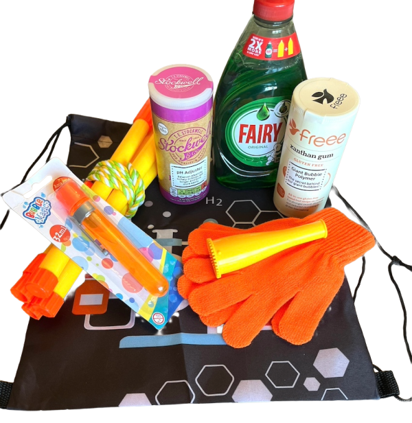 The Bubbleology Science Kit displayed on a surface. The kit includes Fairy Liquid, bicarbonate of soda, xanthan gum, a bubble blower, orange gloves, yellow bubble wands, a tri-string rope wand, and a black Science2Life drawstring bag with a chemistry-themed design.