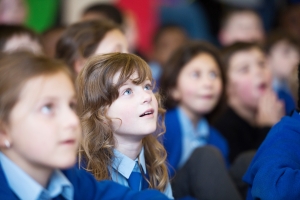 Group of primary school children in blue uniforms watching a bubble show in awe.