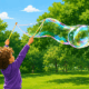 Child using a tri-string bubble wand outdoors to create a giant colourful soap bubble in a park.